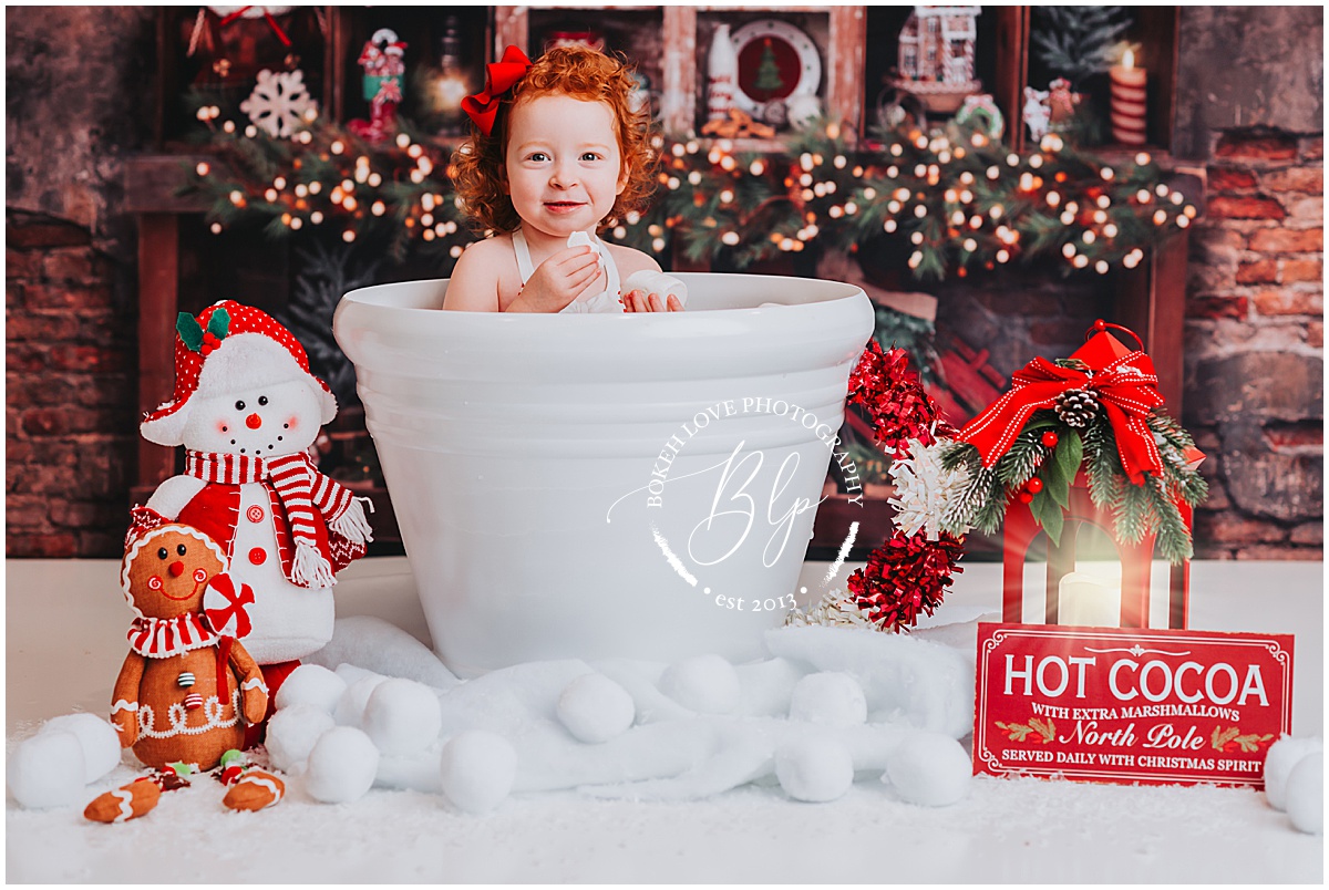 little girl with red curly hair in hot cocoa cup for for Christmas holding a giant marshmallow