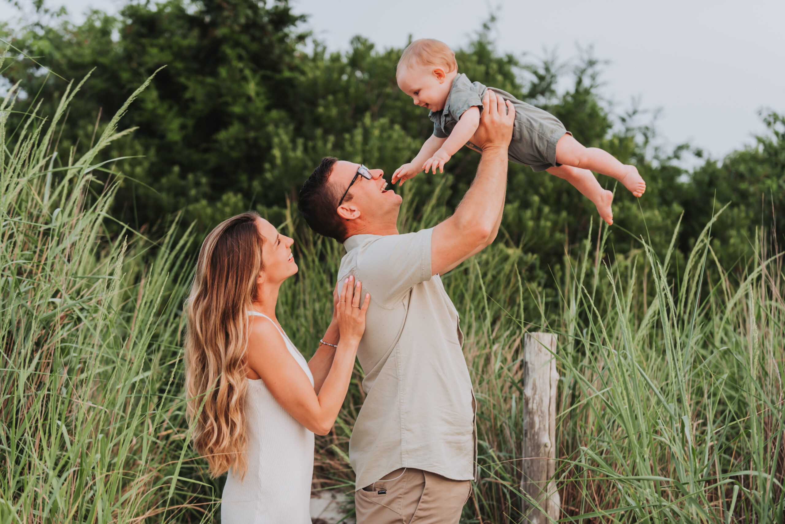 Family holding baby up in front of beach grass with New Jersey beach photographer, Lauren from Bokeh Love Photography