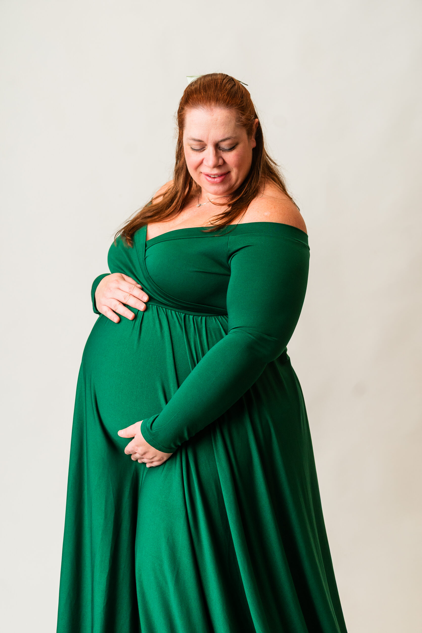 Pregnant mother wearing a green maternity gown during a cozy studio maternity session in South Jersey, photographed on a clean white backdrop