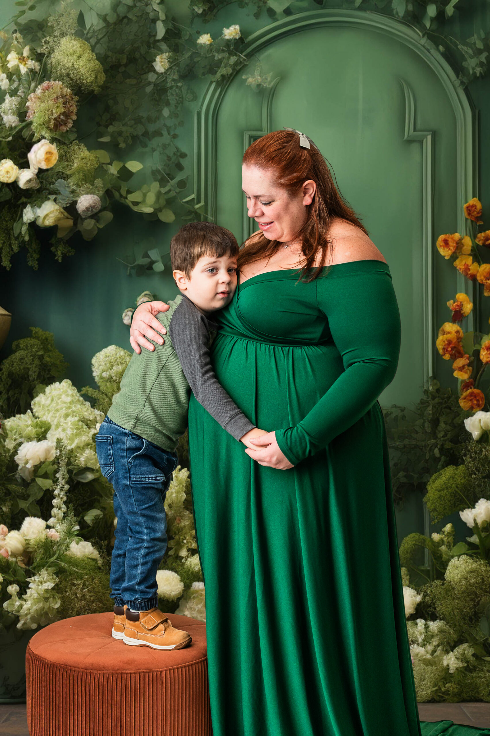 Family maternity image with mom and young son posed in front of a digital green arch with floral details during a South Jersey maternity photography session.