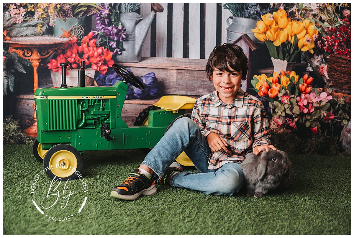 boy sitting in front of spring photography backdrop with gray bunny and toy john deer tractor