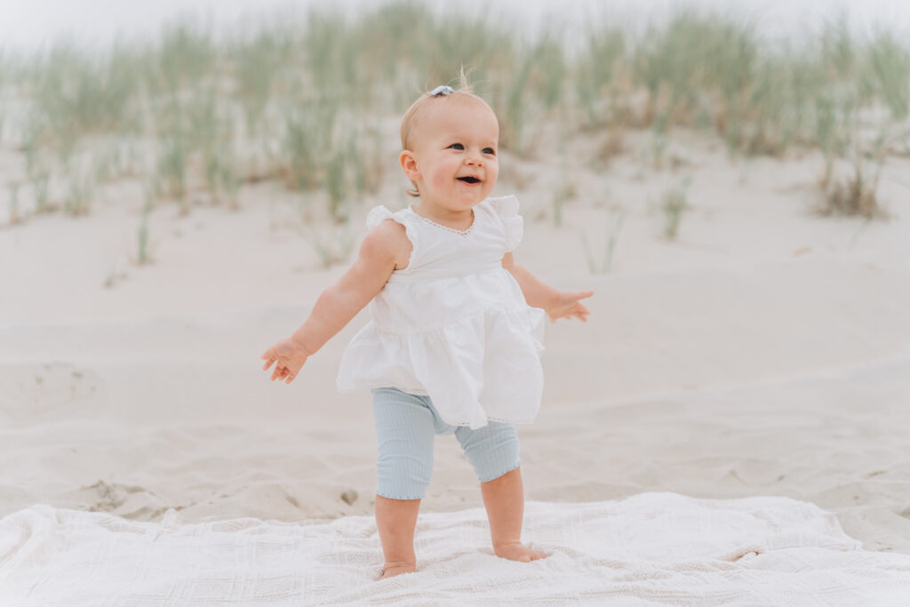 Bokeh Love Photography, Baby photographed on the beach in NJ wearing baby blue capri's and a white ruffled tank top smiling, photos at the Jersey Shore