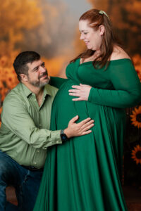 Family maternity photos with mom and dad on a sunflower backdrop during a studio session in South Jersey, showing connection and joy.