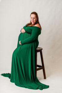 Pregnant mother wearing a green maternity gown during a cozy studio maternity session in South Jersey, photographed on a clean white backdrop.